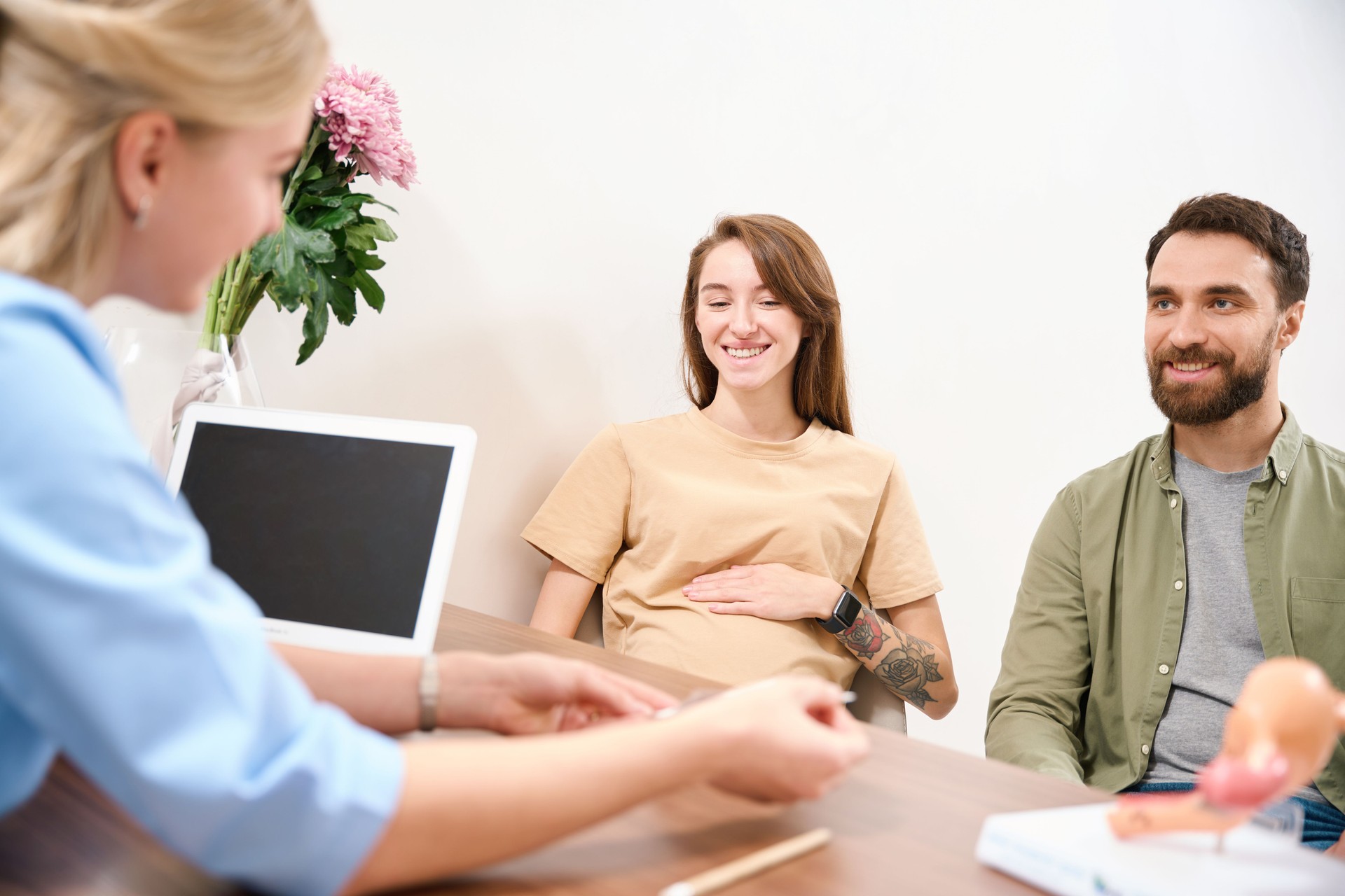 Partial female gynecologist showing something to young smiling pregnant couple