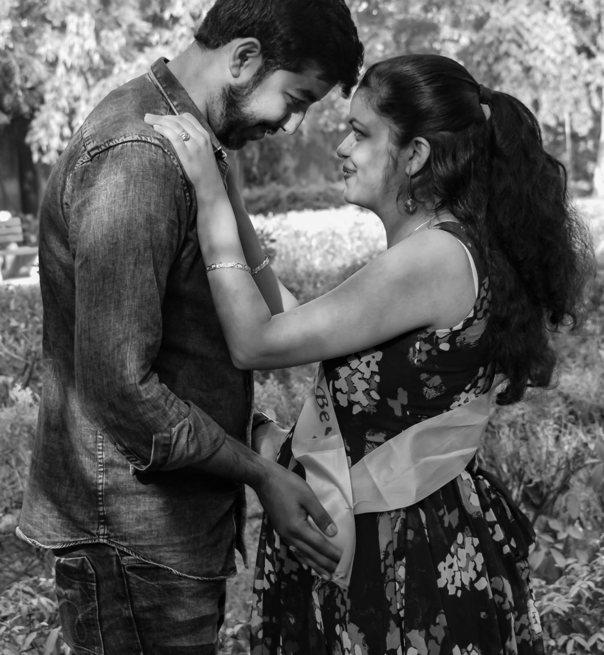 Indian couple posing for maternity baby shoot. The couple is posing in a lawn with green grass and the woman is falunting her baby bump in Lodhi Garden in New Delhi, India - Black and White